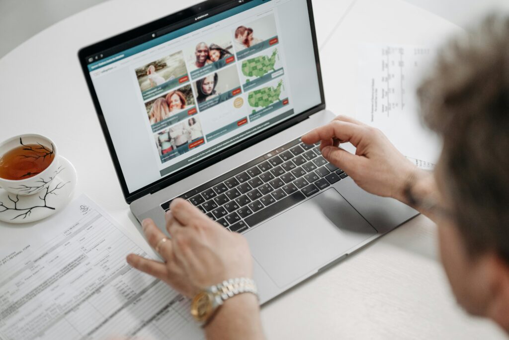 A person browsing a website on a laptop with a cup of tea and documents on a table.