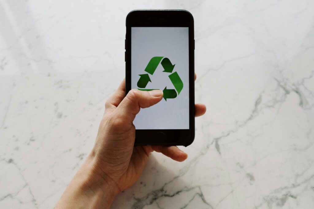 Hand holding smartphone displaying recycling symbol, promoting eco-friendly technology.