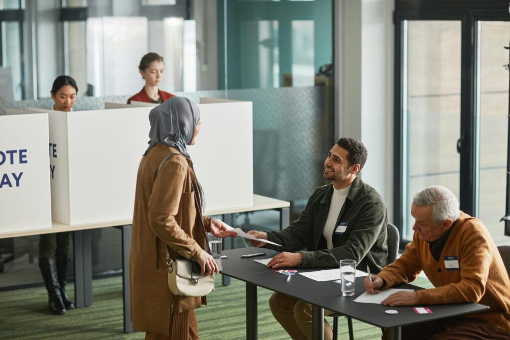 A diverse group of adults participating in a voting process indoors, featuring people of different ethnicities and cultures.