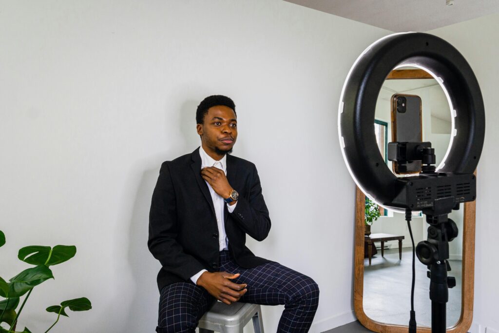 Young man adjusts outfit for a vlog in a modern setup with smartphone and ring light.