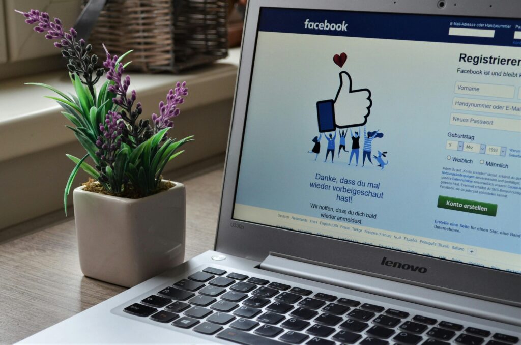 A Lenovo laptop displaying Facebook login beside a lavender plant indoors.