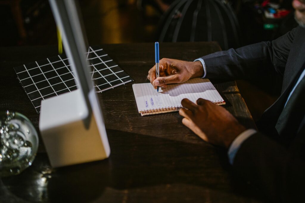 A businessman in a suit writing notes on a notebook at a desk, suggesting a professional office environment.