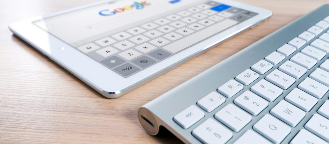 A modern tablet displaying a search engine logo next to a wireless keyboard on a wooden desk.