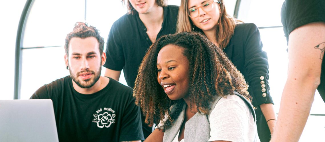 A diverse group of young professionals collaborating around a laptop in a modern office setting. Perfect for business or tech concepts.