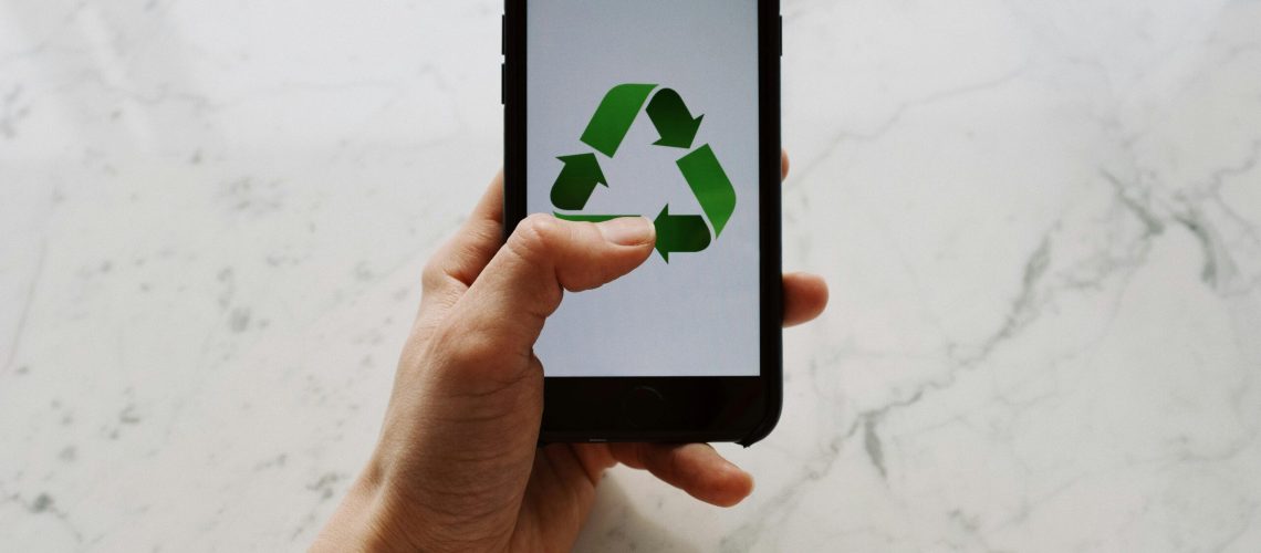 Hand holding smartphone displaying recycling symbol, promoting eco-friendly technology.