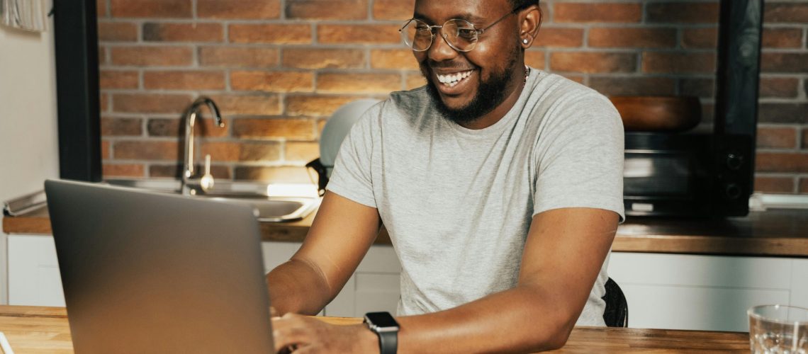 African American man smiling while working remotely on laptop from home office