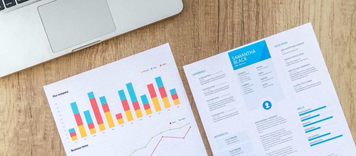 Top view of a laptop, charts, and resume on a wooden desk, showcasing business analysis and job application.