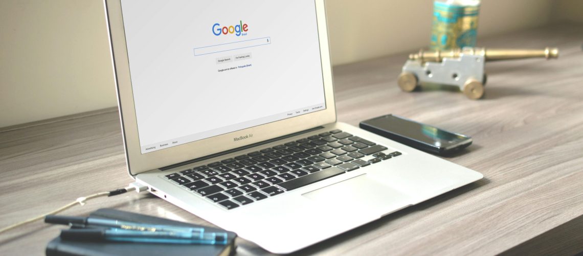 A neat workspace featuring a laptop displaying Google search, a smartphone, and a notebook on a wooden desk.