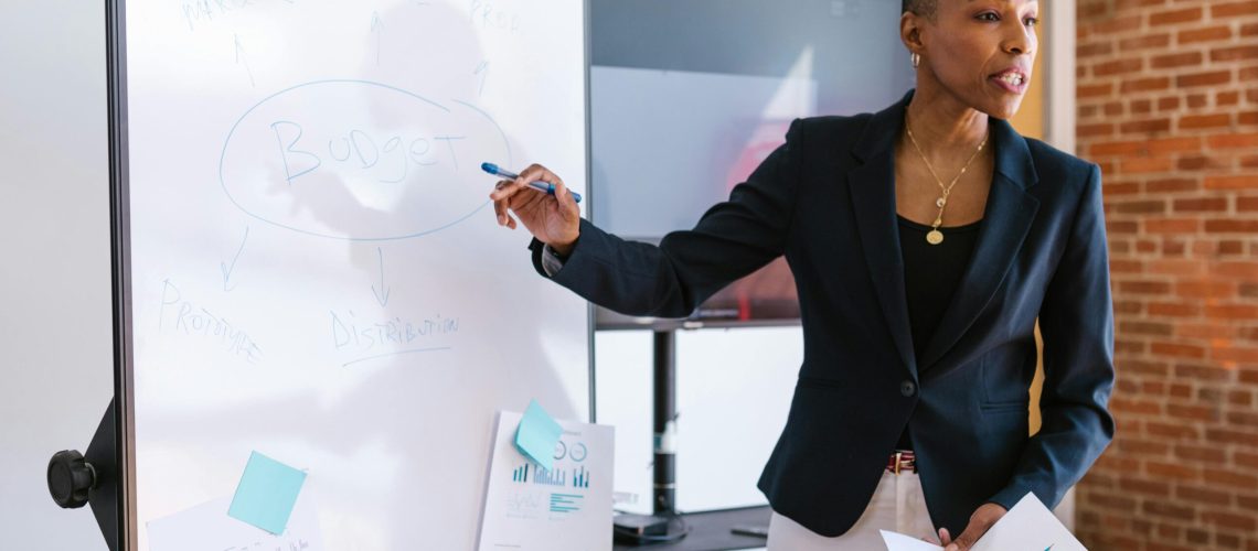 Professional businesswoman explaining budget strategy on a whiteboard during a meeting.