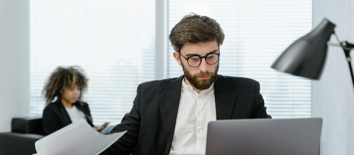 Two business professionals analyzing data on a laptop in a modern office setting, focusing on strategy.