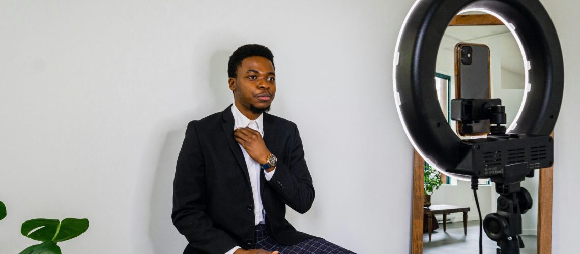 Young man adjusts outfit for a vlog in a modern setup with smartphone and ring light.