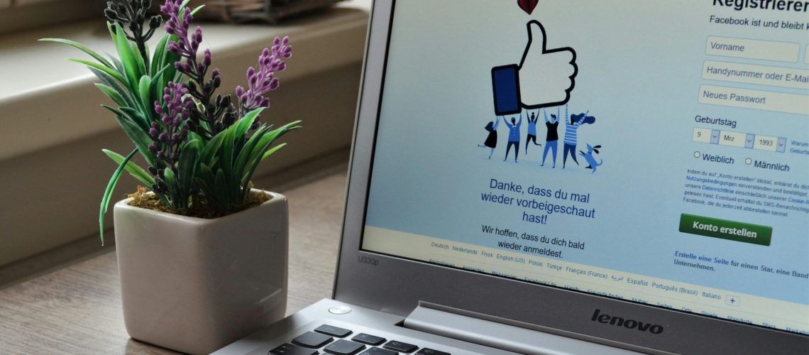 A Lenovo laptop displaying Facebook login beside a lavender plant indoors.